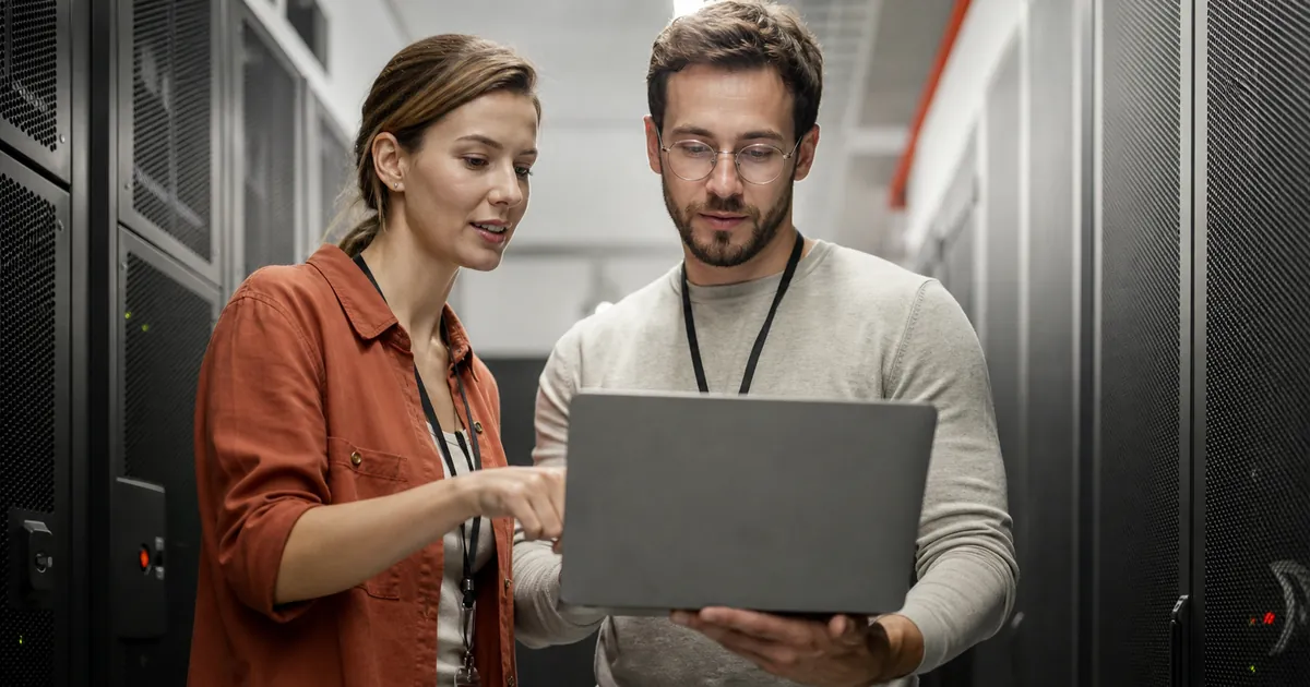 Zwei IT-Fachleute besprechen an einem Laptop im Serverraum die Wahl eines EU-Rechenzentrums