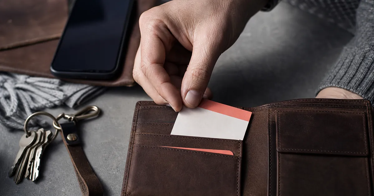 Eine Hand steckt eine laminierte Notfallkarte in ein Portemonnaie neben Schlüsselbund und Smartphone