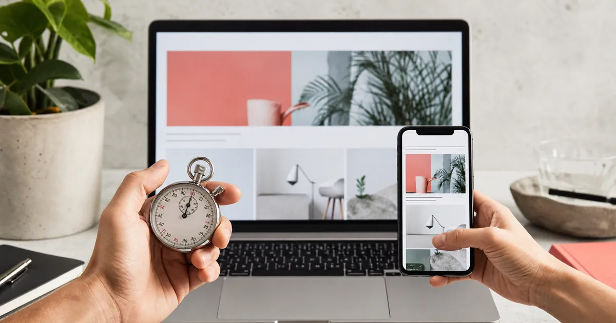 Hände halten Stoppuhr und Smartphone vor einem Laptop mit geöffneter Website als Sinnbild für die Ladezeit