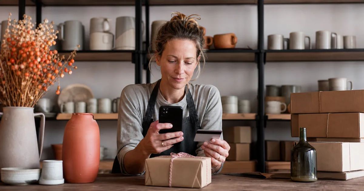 Frau hält Smartphone und Karte neben einem verpackten Paket in ihrem Onlineshop